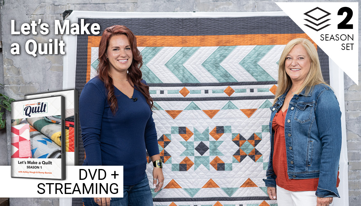Two women standing in front of a hanging quilt