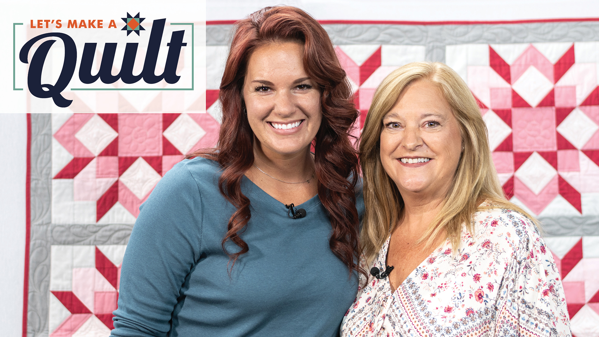 Two women smiling in front of a pink and red quilt
