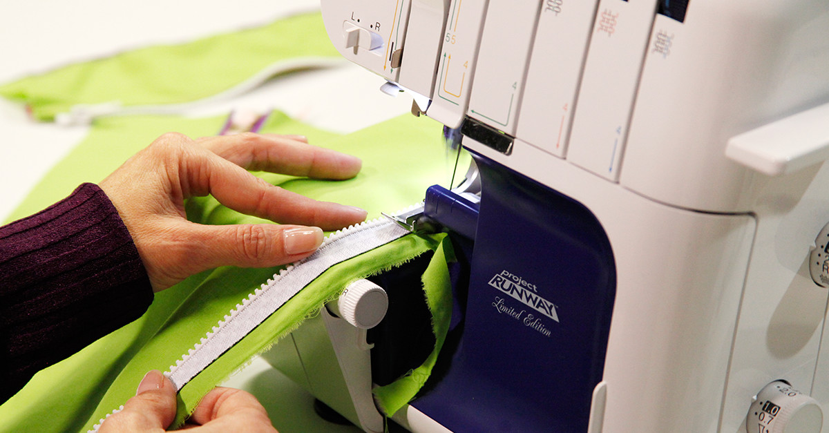 Person sewing a white zipper onto lime green fabric